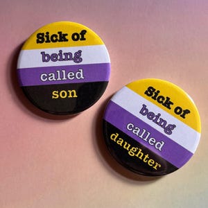 May include: Two circular badges featuring the non-binary pride flag colours: yellow, white, purple, and black. One badge says "Sick of being called son", the other says "Sick of being called daughter".