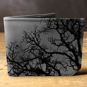 May include: A gray leather wallet with a black silhouette of tree branches printed on the front.