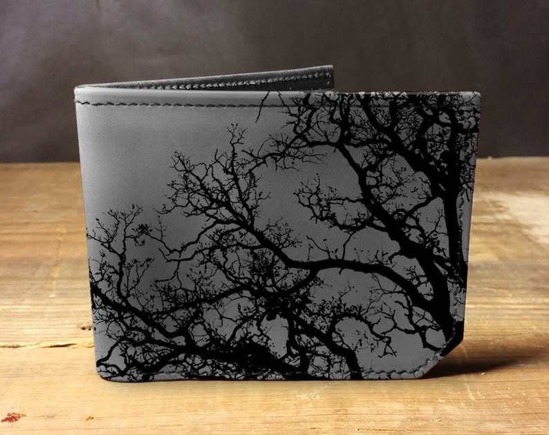 May include: A gray leather wallet with a black silhouette of tree branches printed on the front.