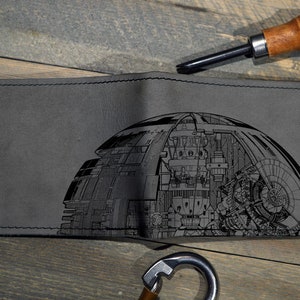 May include: A gray leather wallet with a black and white engraved design of a Death Star from Star Wars.