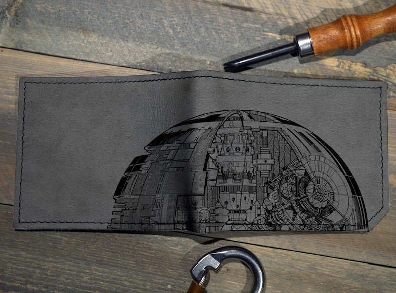 May include: A gray leather wallet with a black and white engraved design of a Death Star from Star Wars.