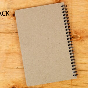 May include: A brown notebook with a black spiral binding. The notebook is lying on a wooden surface.
