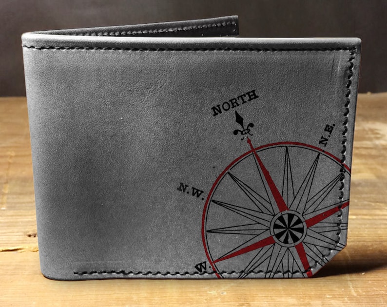 May include: Gray leather wallet with a compass rose design. The compass rose is red and black, with the word "NORTH" above it. The wallet is folded open, showing the interior.