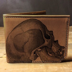 May include: A brown leather wallet with a detailed engraved skull design.