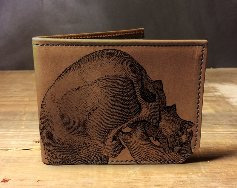 May include: A brown leather wallet with a detailed engraved skull design.