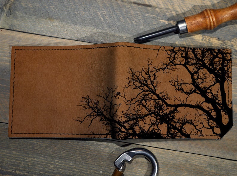 May include: A brown leather wallet with a black silhouette of a tree branch design.