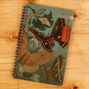 May include: A blue spiral bound notebook with a cover featuring a vintage illustration of moths, butterflies, and caterpillars. The cover also includes the text "Backerton Handmade in the USA".