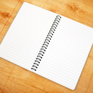 May include: An open spiral bound notebook with lined white pages on a wooden surface.