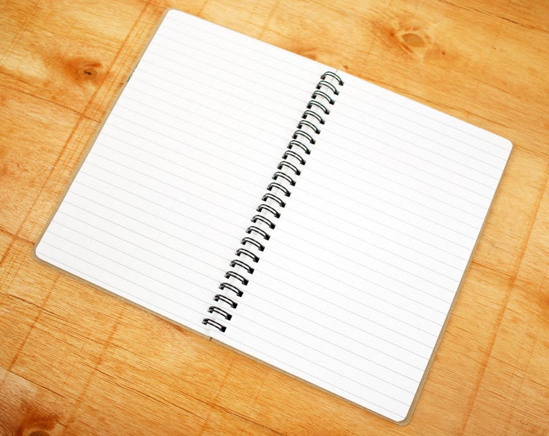 May include: An open spiral bound notebook with lined white pages on a wooden surface.