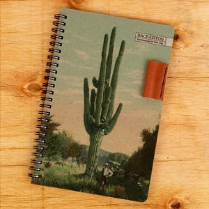 May include: A green spiral bound notebook with a vintage postcard image of a tall cactus. The notebook has a brown leather bookmark and the text "Backerton Handmade in the USA" on the cover.