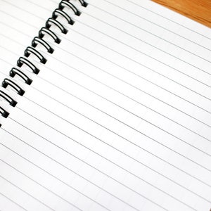 May include: A white spiral bound notebook with lined pages. The notebook is open and the binding is on the left side of the image.