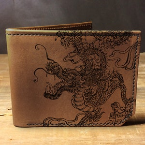 Puede incluir: Una cartera de cuero marr&oacute;n con un dise&ntilde;o de drag&oacute;n negro en relieve en la parte delantera.