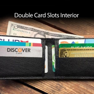 May include: A black leather wallet with two card slots open, showing a Discover card, a blue and green card, and a gold American Express Business card. The wallet is on a wooden surface.