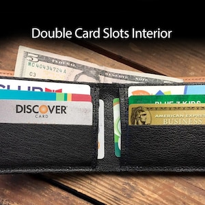 May include: A black leather wallet with two card slots open, showing a Discover card, a blue and green card, and a gold American Express Business card. The wallet is on a wooden surface.