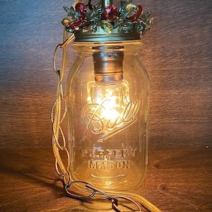 May include: A glass mason jar pendant light with a gold chain and a decorative gold top with red and green accents. The jar is labeled "Ball" and "Perfect Mason".