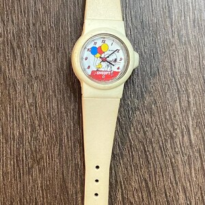 May include: Cream-colored Snoopy wristwatch with a matching band. The watch face features Snoopy holding balloons. The watch band has a buckle closure and multiple adjustment holes. A classic, vintage accessory.
