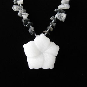 May include: A white carved flower pendant necklace with a silver chain and black and white gemstone beads.