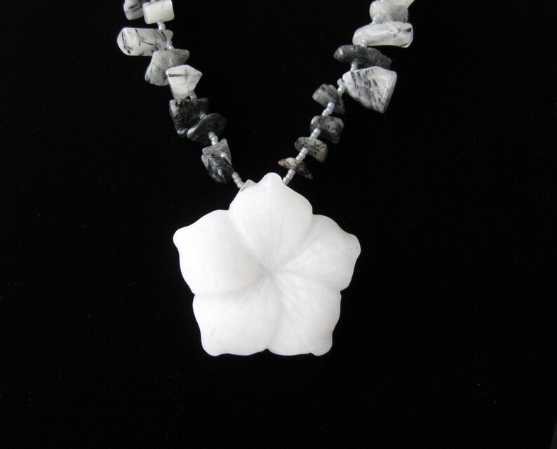 May include: A white carved flower pendant necklace with a silver chain and black and white gemstone beads.