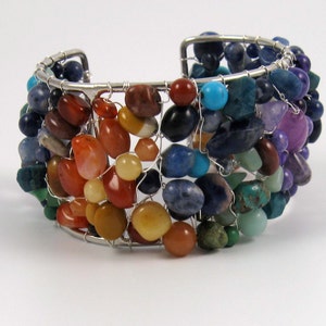 May include: A silver wire wrapped bracelet with a variety of colorful gemstones, including red, orange, yellow, green, blue, and purple.