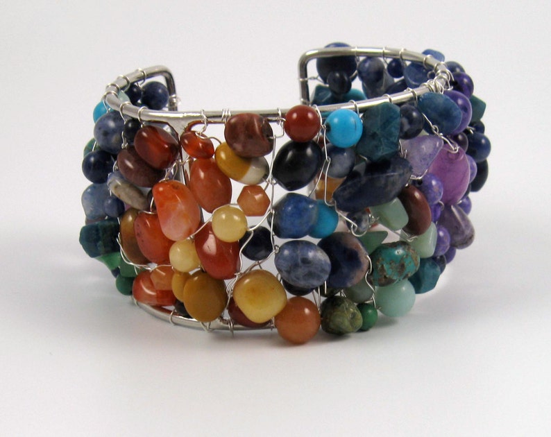 May include: A silver wire wrapped bracelet with a variety of colorful gemstones, including red, orange, yellow, green, blue, and purple.