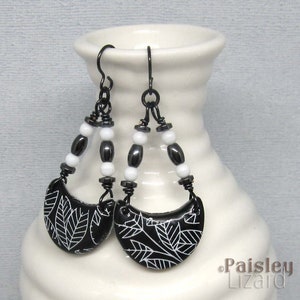 May include: Black and white leaf patterned earrings with black and white beads hanging from black wire.