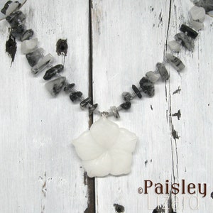 May include: A white flower pendant necklace with a silver chain and black and white gemstone beads.