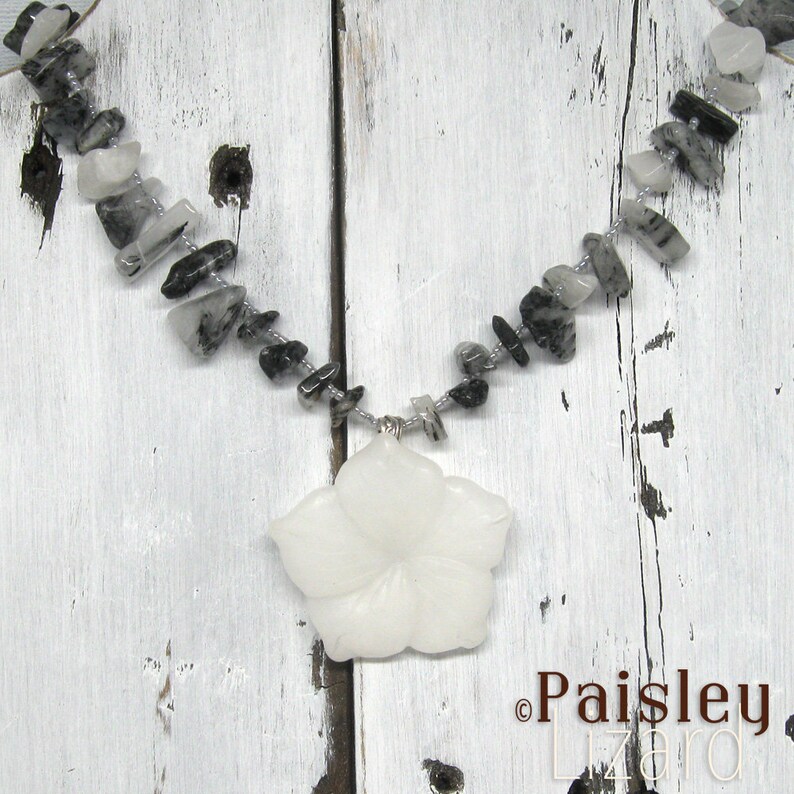 May include: A white flower pendant necklace with a silver chain and black and white gemstone beads.