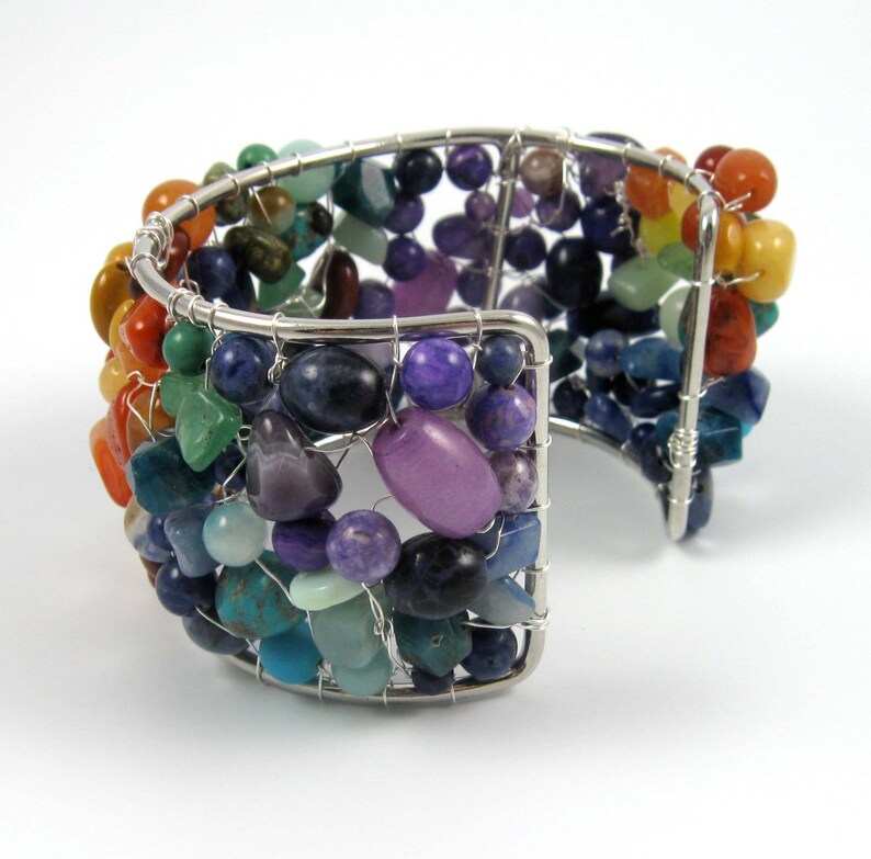 May include: A silver wire wrapped bracelet with a rainbow of semi-precious stones. The bracelet is made with a variety of stones, including amethyst, turquoise, and carnelian.