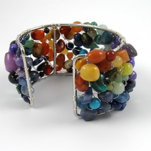 May include: A silver wire wrapped bracelet with a rainbow of colorful gemstones. The bracelet is made with a variety of stones, including amethyst, carnelian, citrine, turquoise, and lapis lazuli.