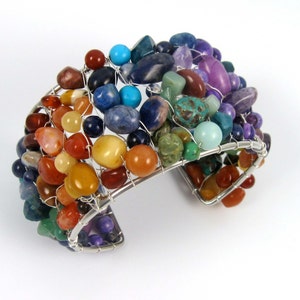 May include: A silver wire wrapped bracelet with a variety of colorful gemstones, including red, orange, yellow, green, blue, and purple.