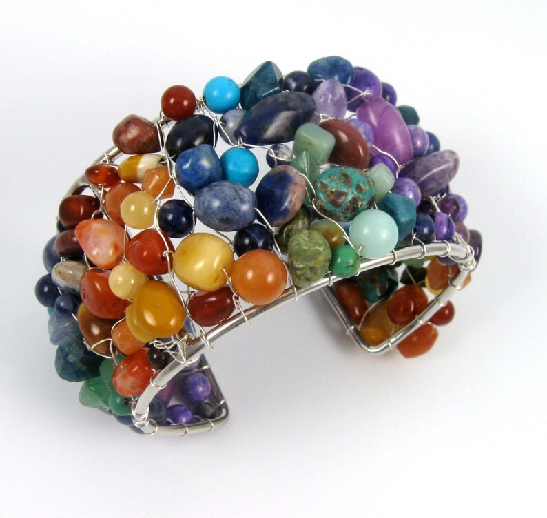 May include: A silver wire wrapped bracelet with a variety of colorful gemstones, including red, orange, yellow, green, blue, and purple.