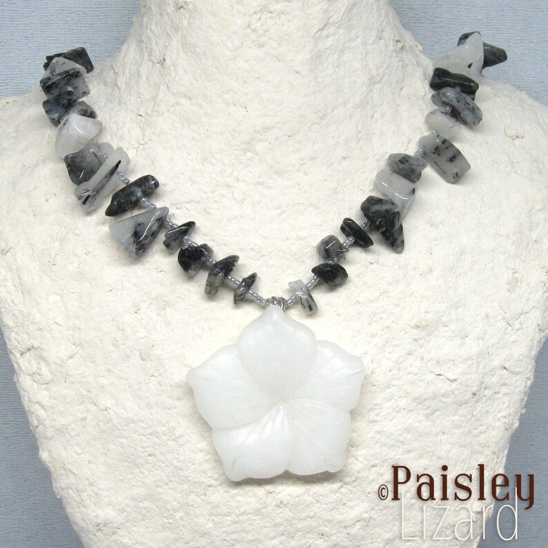 May include: A white flower pendant necklace with a silver chain and black and white gemstone beads.
