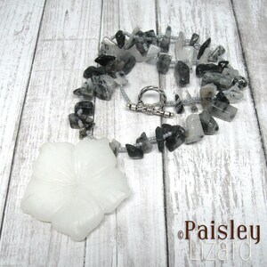 May include: A white flower pendant necklace with a silver clasp. The necklace is made of black and white stones and silver beads.