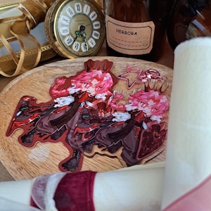 Può includere: Due adesivi in stile anime con un personaggio dai capelli rosa, una corona e un abito rosso e nero. Gli adesivi sono su una superficie di legno, con un orologio da tasca vintage e una bottiglia marrone sullo sfondo.