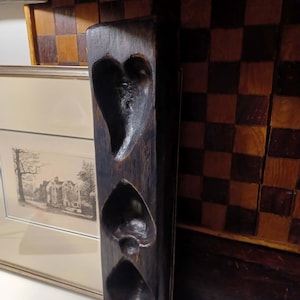May include: A dark brown wooden mold with three carved shapes: a heart, a spade, and a diamond. The mold is rectangular and stands vertically. The background includes a framed picture and a checkered pattern.