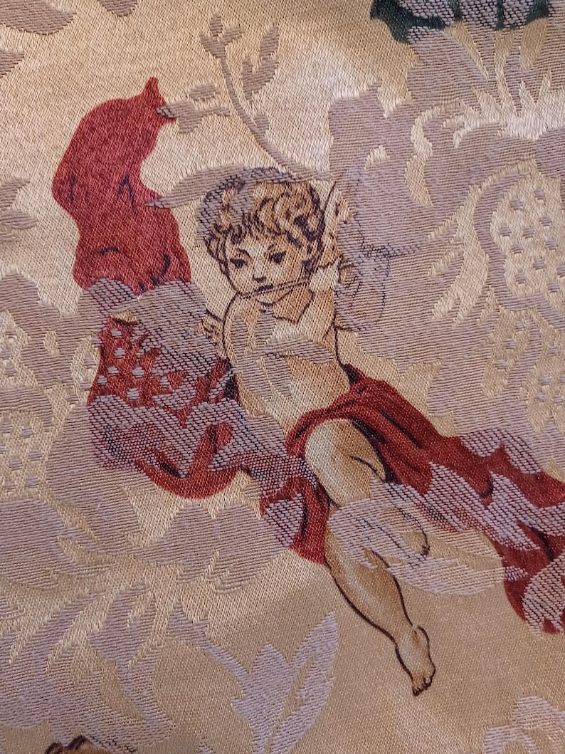 K&ouml;nnte beinhalten: Nahaufnahme eines gewebten Stoffes mit einem Cherub-Design. Der Cherub ist mit heller Haut, lockigem Haar und einem roten Tuch dargestellt. Der Hintergrund hat ein Blumenmuster in Beige und Hellviolett.