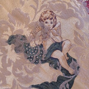 K&ouml;nnte beinhalten: Nahaufnahme eines Wandteppichs mit einem Cherub, der Fl&ouml;te spielt. Der Cherub hat Fl&uuml;gel und sitzt auf einer Wolke. Der Hintergrund ist ein Blumenmuster in Gold-, Beige- und Gr&uuml;nt&ouml;nen.