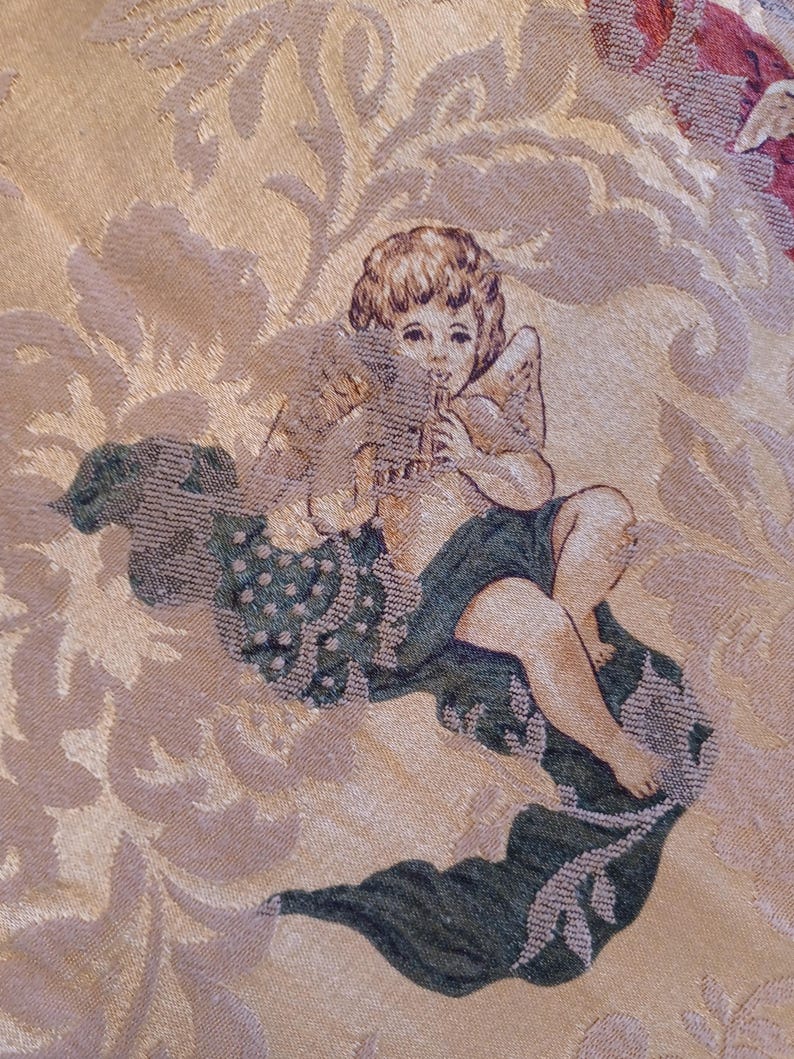 K&ouml;nnte beinhalten: Nahaufnahme eines Wandteppichs mit einem Cherub, der Fl&ouml;te spielt. Der Cherub hat Fl&uuml;gel und sitzt auf einer Wolke. Der Hintergrund ist ein Blumenmuster in Gold-, Beige- und Gr&uuml;nt&ouml;nen.