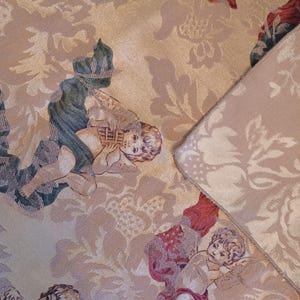 K&ouml;nnte beinhalten: Nahaufnahme eines beigefarbenen Stoffes mit einem sich wiederholenden Muster aus Cherubinen und floralen Designs. Die Cherubinen sind in verschiedenen Posen dargestellt, mit Details in Gr&uuml;n, Rot und Beige. Der Stoff hat ein strukturiertes Aussehen.