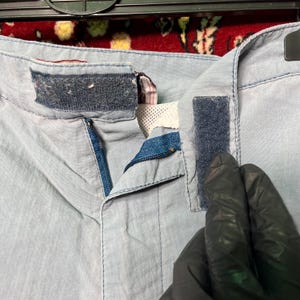 Puede incluir: Primer plano de unos pantalones cortos azul claro con cremallera y cierres de velcro. Los pantalones cortos est&aacute;n hechos de una tela ligera y tienen una cremallera azul. Los cierres de velcro son de color azul oscuro.