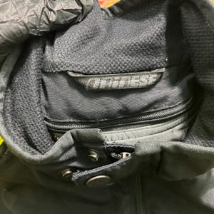 May include: Close-up of a black motorcycle jacket with a high collar and a zipper closure. The jacket has a mesh lining and the brand name "Dainese" is visible on a label near the collar.