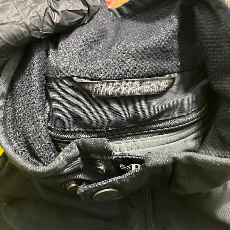 May include: Close-up of a black motorcycle jacket with a high collar and a zipper closure. The jacket has a mesh lining and the brand name "Dainese" is visible on a label near the collar.