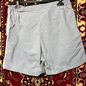 Puede incluir: Pantalones cortos deportivos de color azul claro con cintura el&aacute;stica y un peque&ntilde;o logotipo azul. Los pantalones cortos est&aacute;n hechos de un material ligero, posiblemente nailon. Los pantalones cortos est&aacute;n colgados en una percha negra.