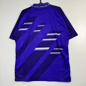 Puede incluir: Una camiseta de f&uacute;tbol vintage del Real Madrid en azul real, con rayas diagonales en azul oscuro y blanco. El cuello muestra "REAL MADRID" en blanco. La camiseta tiene mangas cortas y un dise&ntilde;o deportivo cl&aacute;sico.