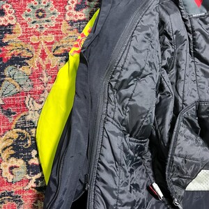 May include: Close-up of a black motorcycle jacket with a quilted interior. The jacket has a zipper closure and a bright yellow lining visible on the left side. The jacket is made of a durable material.