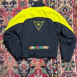May include: Black and yellow motorcycle jacket with the text "THE DOCTOR" in colorful letters. The jacket has a yellow upper section and a black lower section. A yellow triangle logo is on the back.