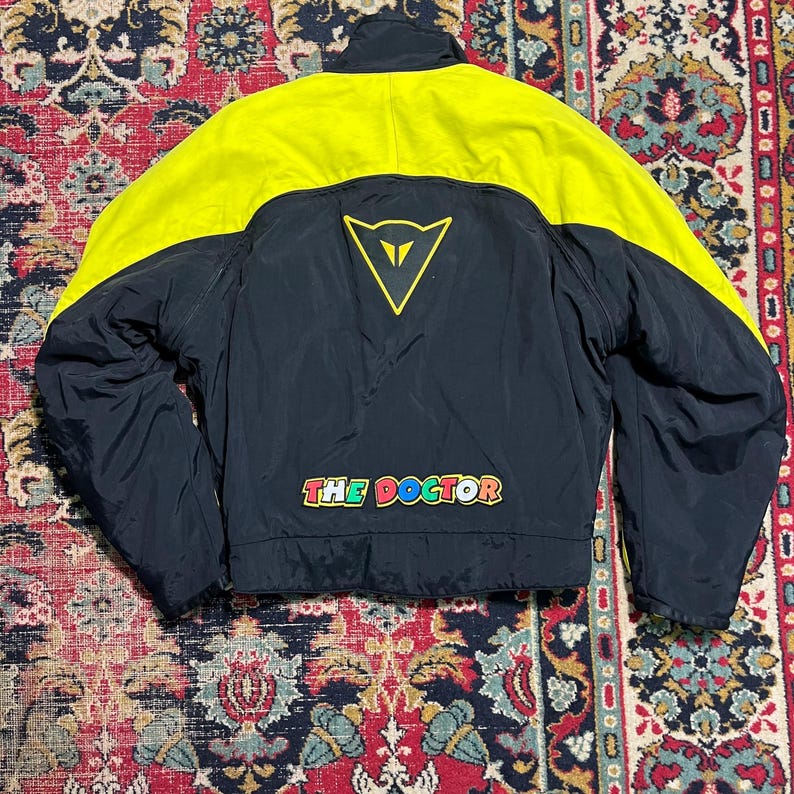 May include: Black and yellow motorcycle jacket with the text "THE DOCTOR" in colorful letters. The jacket has a yellow upper section and a black lower section. A yellow triangle logo is on the back.