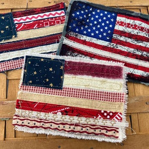 May include: Three rectangular fabric patches featuring American flag designs. Each patch is constructed from various textile strips including red, white, and blue patterns, stars, and gingham, with frayed edges and visible stitching throughout.