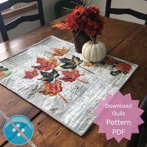 Pode incluir: Um corredor de mesa acolchoado branco com um fundo de impressão de jornal e folhas de outono coloridas. O corredor de mesa está sobre uma mesa de madeira com uma abóbora branca e um vaso de flores vermelhas.