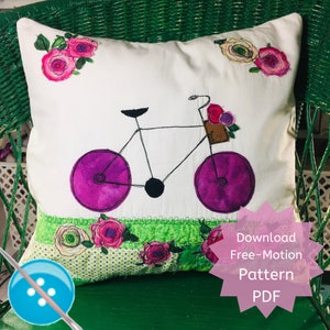 May include: A white pillow with a purple bicycle design and pink flowers embroidered on it. The pillow is sitting on a green wicker chair. The text "Download Free-Motion Pattern PDF" is on a pink starburst.